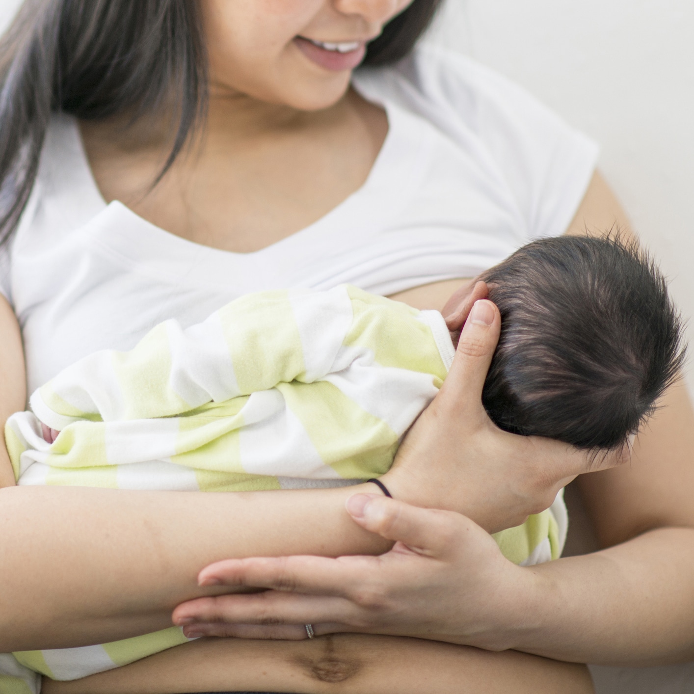 A mother and newborn baby boy are indoors together. The mother is breastfeeding her baby.