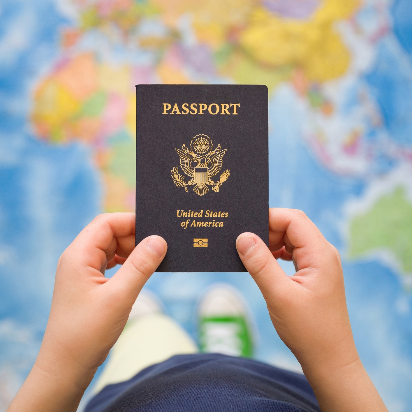 Child's hand holding US passport. Map background. Ready for traveling. Open world.
