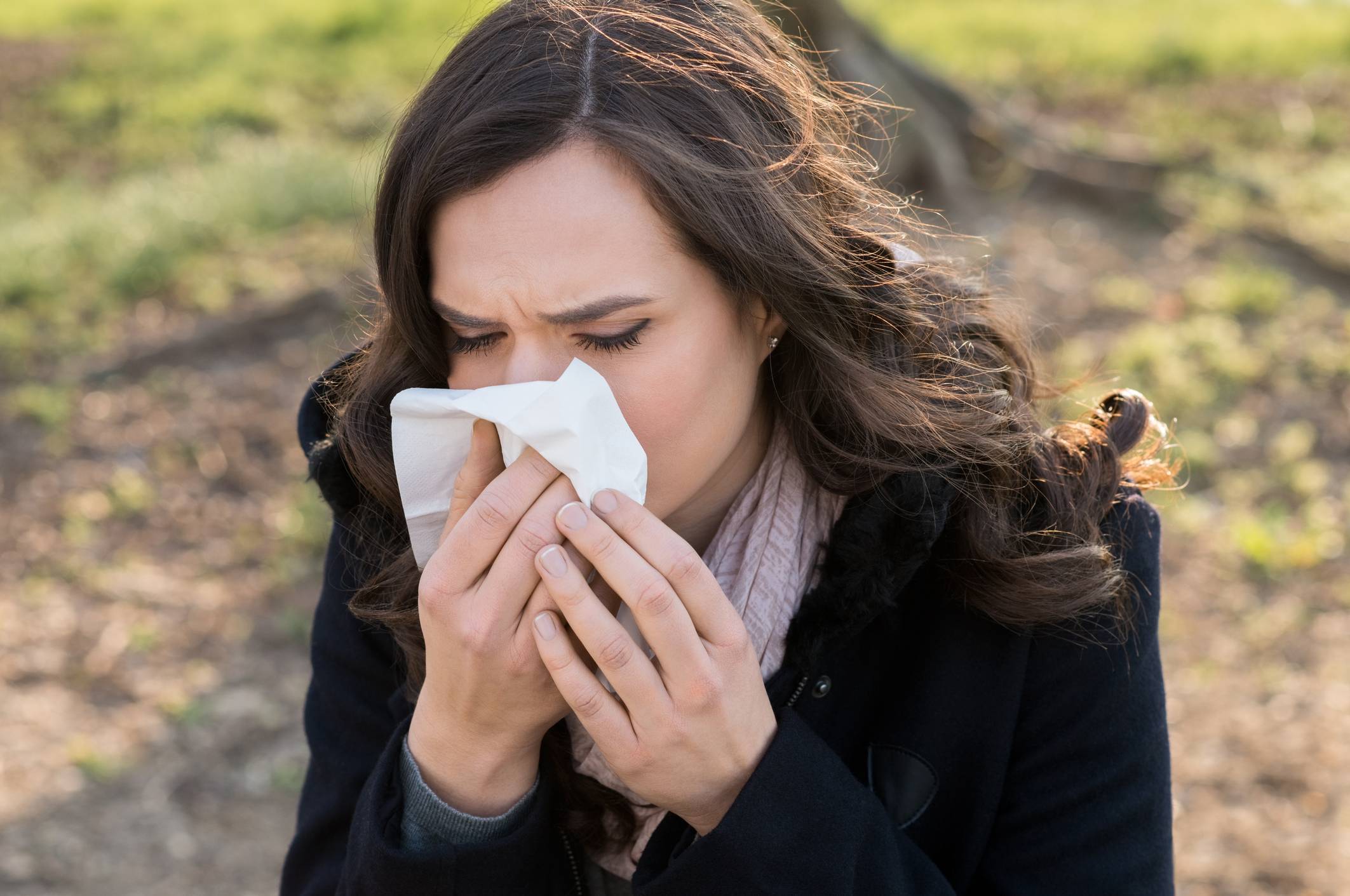 woman sitting outside and blowing her nose because sinus infection season