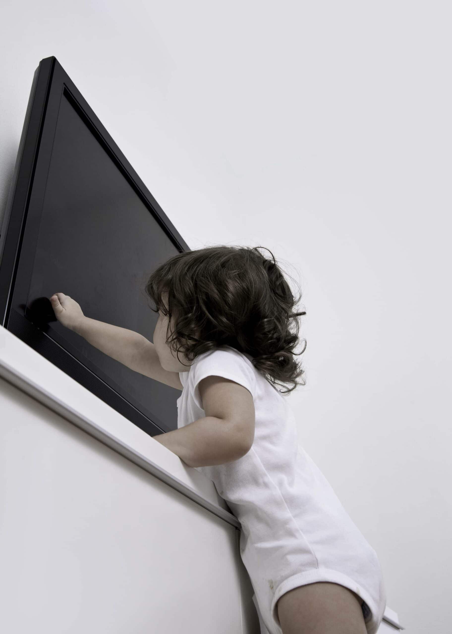 Little girl reaching up to touch the TV