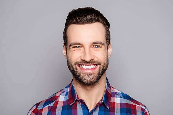 man with plaid shirt smiling at camera with grey background