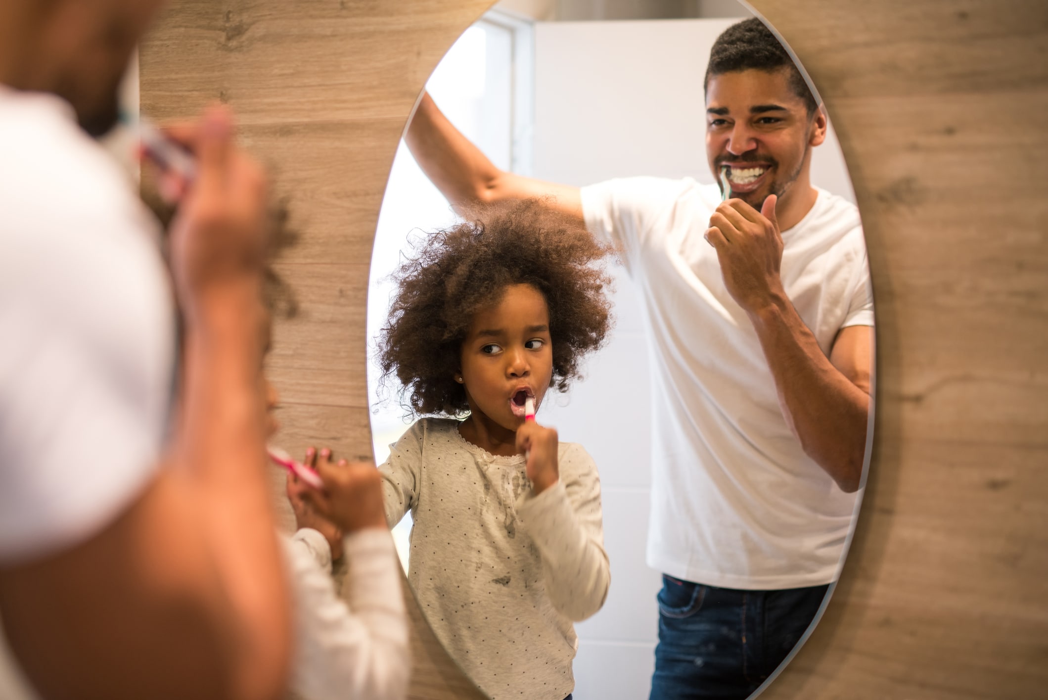 dad and daughter brushing teeth together in the bathroom mirror