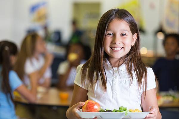 Cute Hispanic elementary school student holding tray of cafeteria food