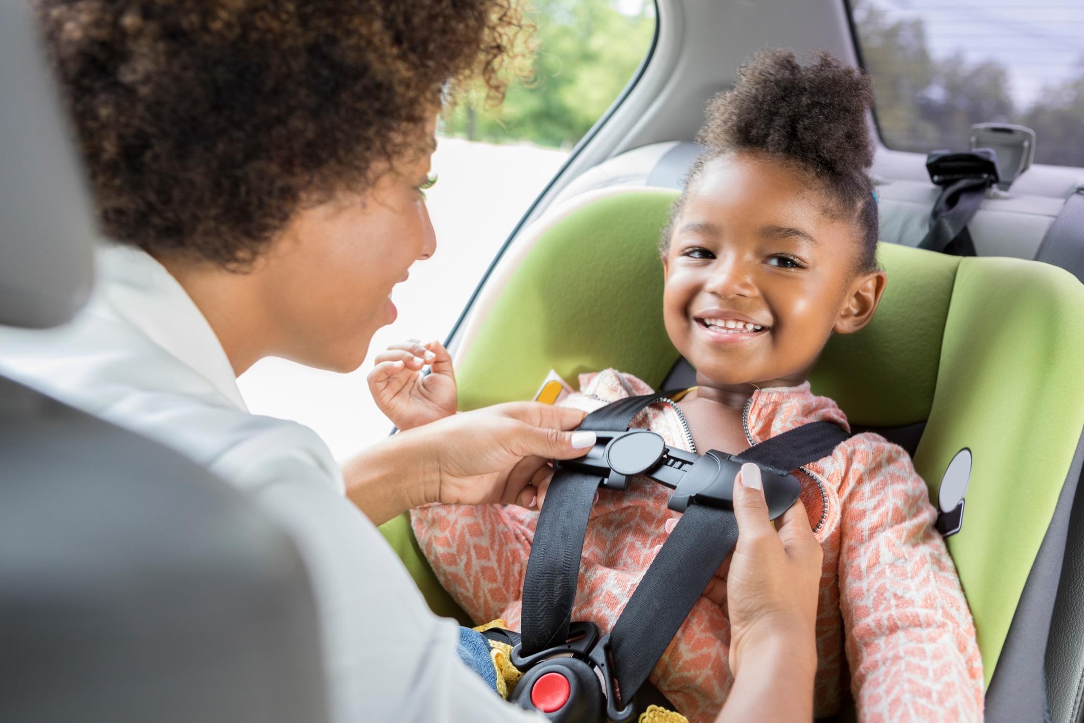 woman buckling up child in green car seat