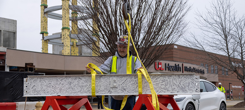 Construction worker prepares white steel beam to be hoisted in to UofL Health – South Hospital construction site.