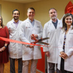 Ear, Nose & Throat (ENT) physicians in white lab coats holding red ribbon and large scissors.