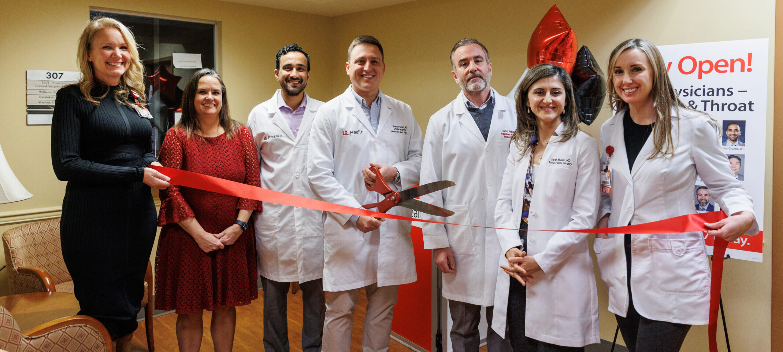 Ear, Nose & Throat (ENT) physicians in white lab coats holding red ribbon and large scissors.