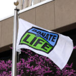 White flag with blue and green Donate Life logo blowing in the wind.