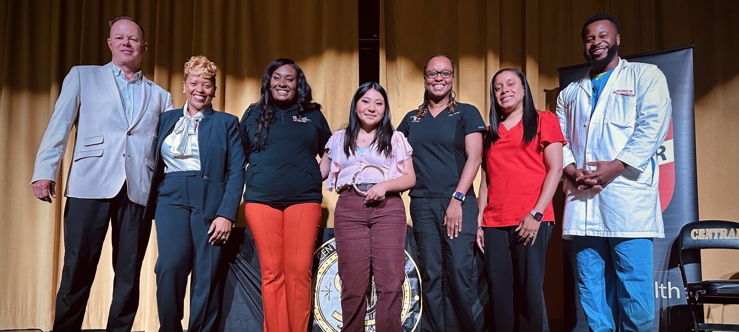 Central High School Student Jocelyn Vasquez poses with the UofL Health and Central High School leadership teams. Jocelyn (center) is holding the Award for Outstanding Service in Trauma Response she received.