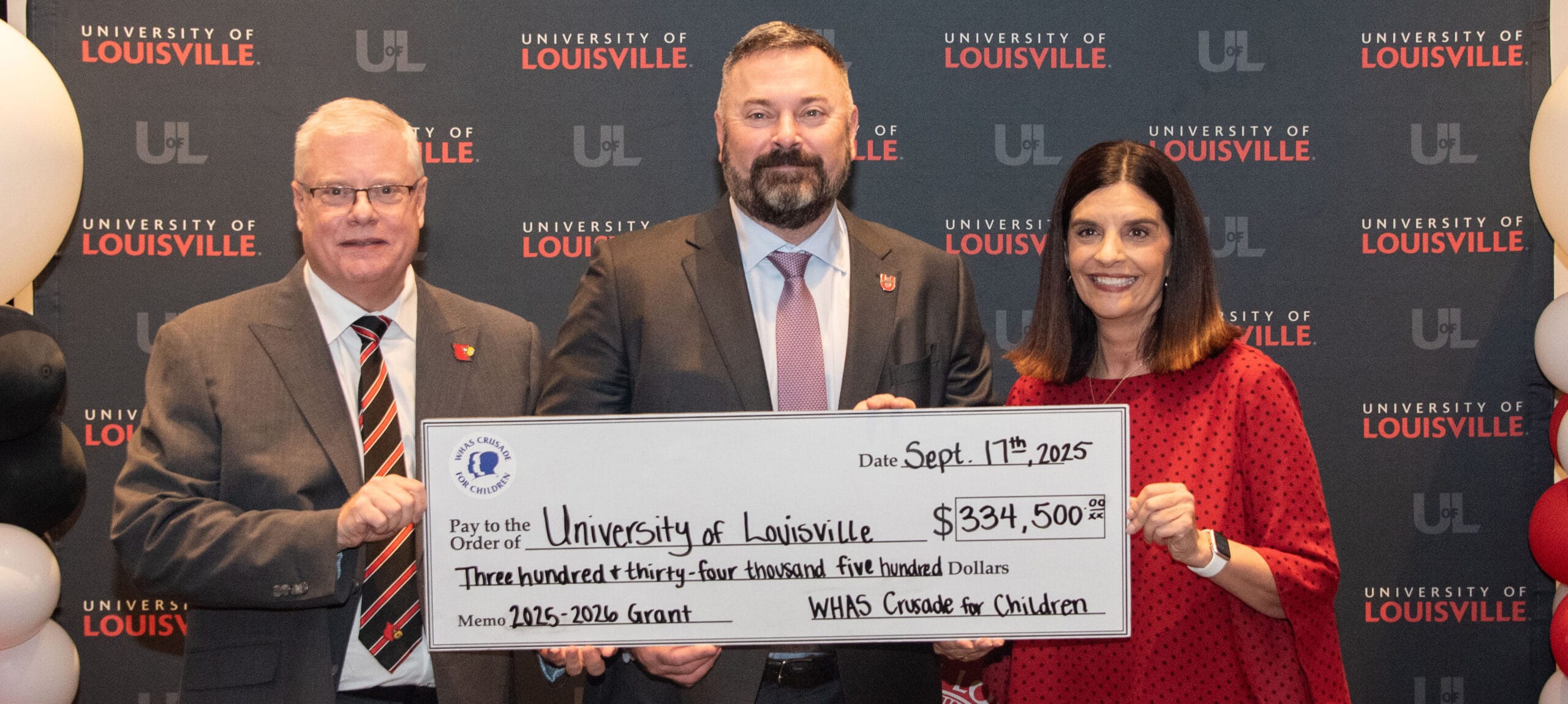Three individuals stand behind a large check addressed to the University of Louisville for $334,500 from the WHAS Crusade for Children.